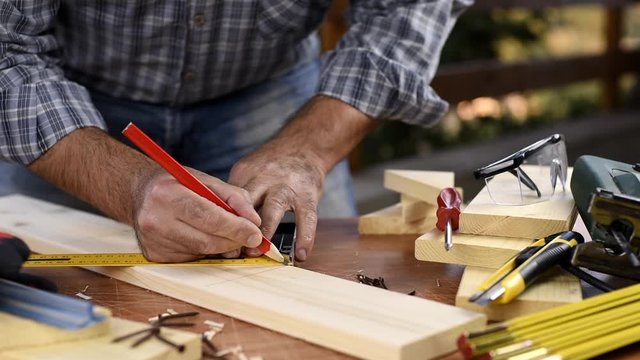 Adult carpenter craftsman with a pencil and the carpenter's square trace the cutting line on a wooden table. Construction industry, housework do it yourself. Footage.