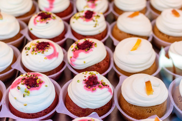 Group of freshly cooked cakes with whipped cream and fruits, displayed for sale at an weekend street market, selective focus