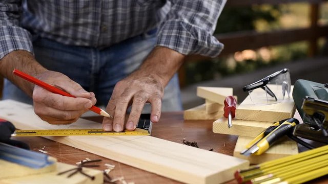 Adult carpenter craftsman with a pencil and the carpenter's square trace the cutting line on a wooden table. Construction industry, housework do it yourself. Footage slow motion.