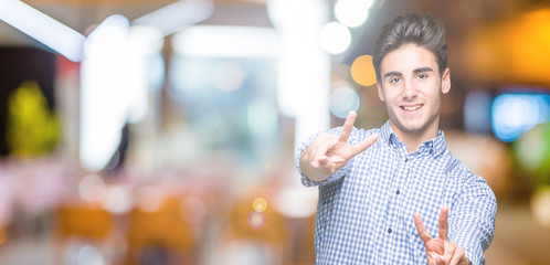 Young handsome business man over isolated background smiling looking to the camera showing fingers doing victory sign. Number two.