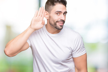 Young man wearing casual white t-shirt over isolated background smiling with hand over ear listening an hearing to rumor or gossip. Deafness concept.