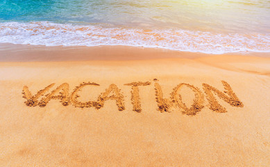 Vacation text on a beach. Vacation written in a sandy tropical beach. "Vacation" written in the sand on the beach blue waves in the background. Vacation on the sand beach concept.