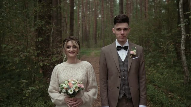 A beautiful girl and a guy in wedding dresses stand and look into the camera. Average plan. Wedding couple with smiles looking at the camera