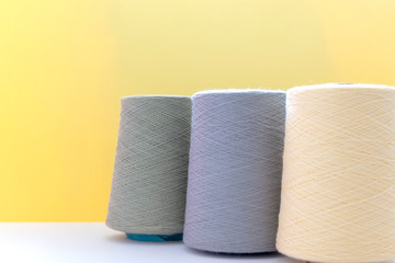 Pastel color bobbins of wool yarn for hand and machine knitting on a yellow background