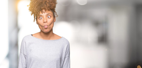 Beautiful young african american woman over isolated background making fish face with lips, crazy and comical gesture. Funny expression.