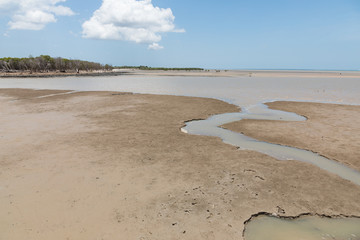 coastal mudflat at low tide with water running through and blue sky