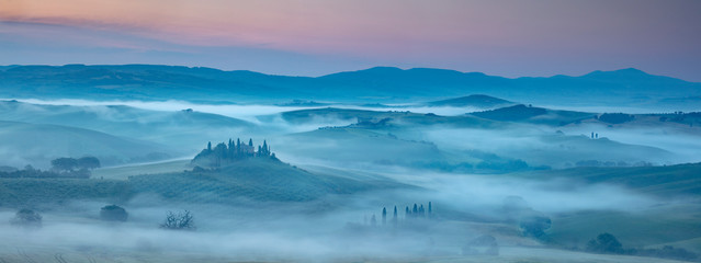 Tuscany Misty dawn over farmhouses, vineyards olive groves & trees of Val D'Orcia San Quirico south of Pienza Tuscany Italy
