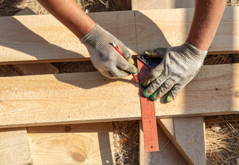 Worker measures a wooden board at a construction site