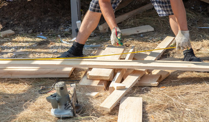 Worker measures a wooden board at a construction site