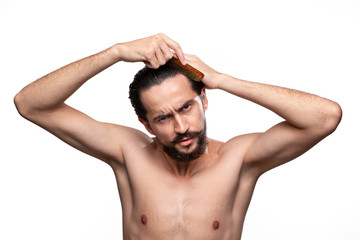 Fototapeta premium Stylish handsome bearded with mustaches combing hair standning bare isolated over white background. Concept of morning treatment. Morning routine