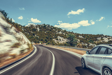 White car moves on the road among the mountains and forests.