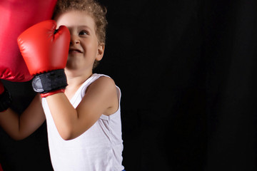 A little boy in red boxing gloves trains to hit the boxing bag. Sports, children's boxing.