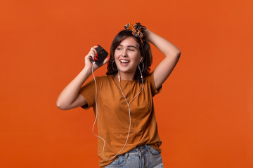 Pretty brunette woman in a t-shirt and beautiful headband dancing listening to music with wired headphones isolated over orange background. Enjoying life