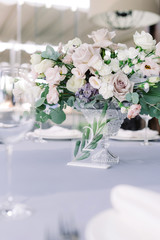 Stylish decoration of modern wedding with fresh flowers and table number on a small glass stand.