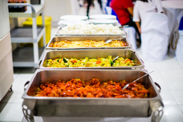 Array of dishes in stainless steel trays, like sweet and sour meat, chop suey, spaghetti, rice. Selective focus. Copy space.