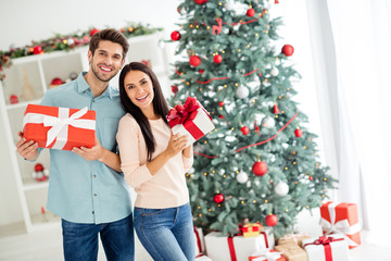 Portrait of two enthusiastic people having brunette hair hold gifts packages enjoy christmas time follow x-mas tradition in house indoors