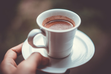 Hand holding a homemade hot yummy chocolate in a white ceramic cup. Personal perspective.