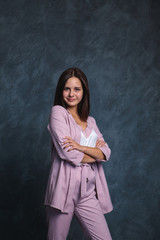 Fototapeta na wymiar Business woman in a light suit on a dark background stands and looks at the camera and smiles. Portrait of a business girl on a gray background, space for text.