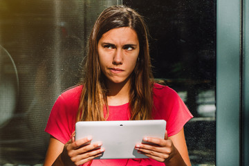 Young female doubting and thinking while using a digital tablet