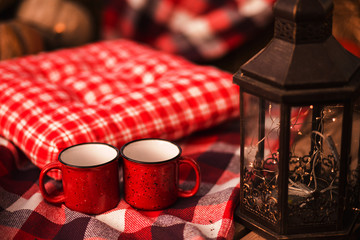 Two red cups of coffee in the park at picknic on red checkered cover at autumn background.
