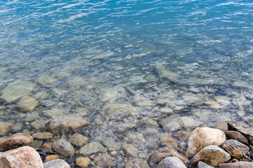 Pebbles and rocks on beach with pure blue transparent water background