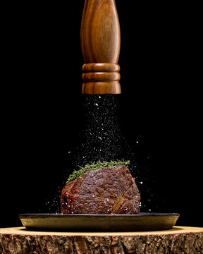 Roasted beed from grill in cast iron skillet on wooden plate. Salt strewing from the mill