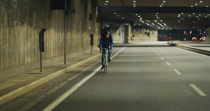 Slow motion of an young delivery courier with bicycle is touching a futuristic screen with augmented reality hologram maps to view the addresses of customers in the evening in a city center.