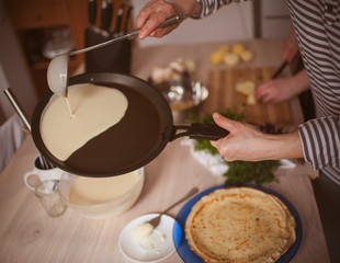 A woman is preparing pancakes for Easter at home kitchen using frying pan.