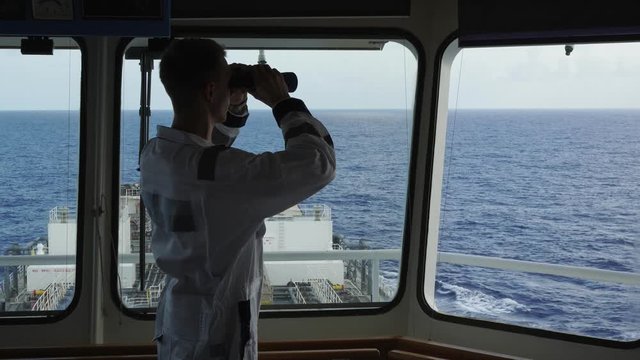watch officer looks at ocean water through black binoculars on captain bridge