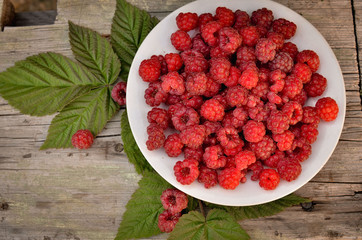 Fresh beautiful raspberries lie that dish in the park. Raspberries and its leaves in a still life. Bright summer photo in warm tint.