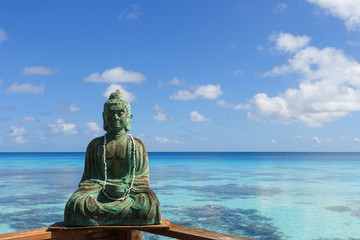 A sculpture of Buddha rests on a railing overlooking a tropical lagoon on the island of Fakarava in French Polynesia