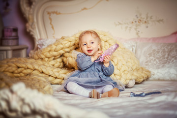 Portrait of a little beautiful girl in a gray dress who is sitting on the bed and laughing. Copy space