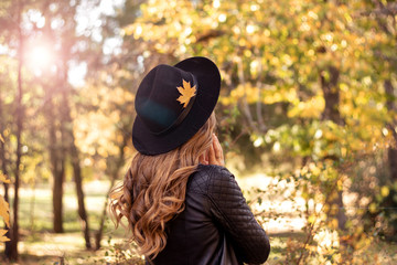 Autumn fashion lifestyle concept. Beautiful young European woman with natural fair hair in a black hat walking in autumn park