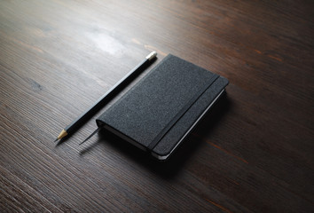 Black notebook and pencil on wooden background. Responsive design mockup.