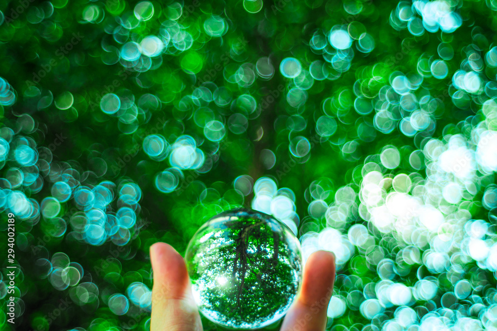 Wall mural Mobile crystal ball with green backdrop from leaves and bokeh from natural light.