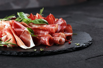 Marble cutting board with prosciutto, bacon, salami and sausages on wooden background. Rustic Meat platter