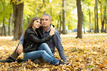 Love couple sitting  on yellow leaves in autumn park. Happy man and woman hugging, enjoying good weather, romantic date, autumn leisure.