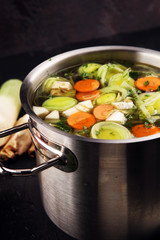 Broth with carrots, onions various fresh vegetables in a pot - colorful fresh clear spring soup. Rural kitchen scenery vegetarian broth