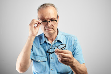 Old man in eye glasses with diopters squints, stares intently at the camera isolated on a white...