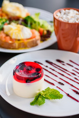 Tasty Panakota dessert on round white plate on table in restaurant. Creamy strawberry dessert. Close-up. Space