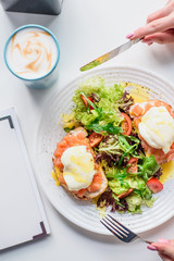 Girl eats toasts with salmon and poached egg, served with fresh salad in restaurant. Healthy breakfast. Close-up. Space. Series of photos