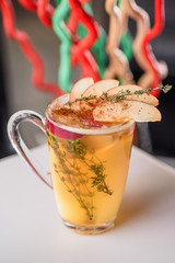 Autumn tea with rosemary, cinnamon, decorated with apple slices in transparent cup on white table in restaurant. Close-up. Space