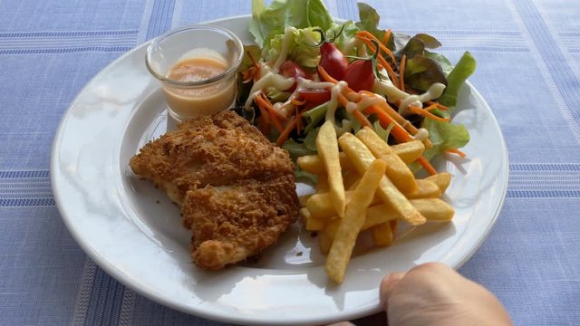 Deep fried fish steak served with french fries and fresh vegetables on white plate