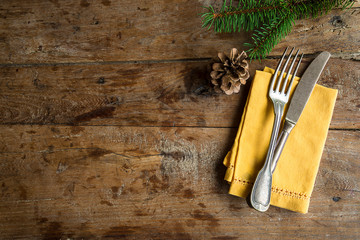 Vintage cutlery on the yellow napkin and fir branch with cone on the old wooden background with...