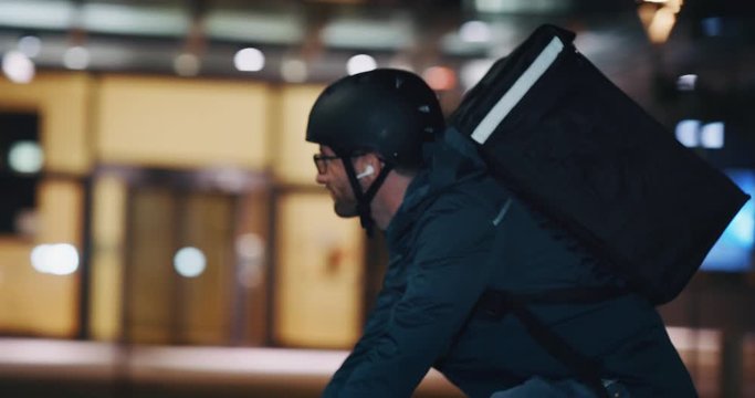Slow motion of an young delivery courier with bicycle is touching a futuristic screen with augmented reality hologram maps to view the addresses of customers in the evening in a city center.