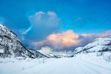 Arctic ice road covered in snow leads to a valley between hills at sunset