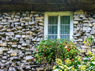 Fototapeta na wymiar Altes Haus aus groben Steinen mit Fenster und Blumenschmuck
