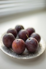 Ripe purple plums in a silver plate. Fresh fruits on the white table. Side view
