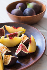 Slices of figs and peaches are in a clay plate on a light wooden table . Autumn fruits. Vegetarianism. Detox diet. Healthy snack