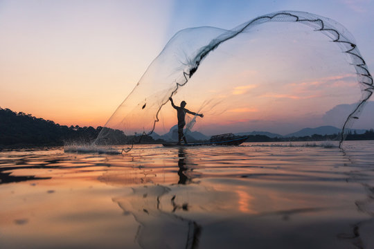 Asian fishermen throwing fishing net during twilight on wooden boat at the lake. Concept Fisherman's Lifestyle in countryside. Lopburi, Thailand, Asia